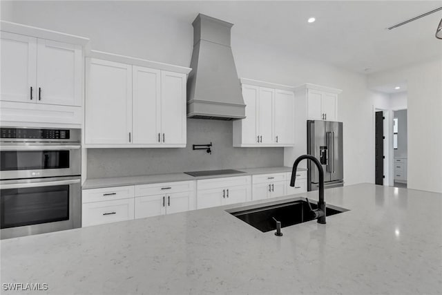 kitchen featuring appliances with stainless steel finishes, light stone countertops, white cabinets, sink, and custom exhaust hood