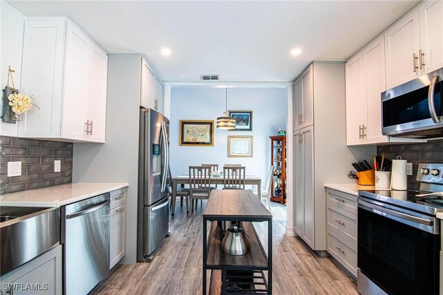 kitchen featuring tasteful backsplash, light hardwood / wood-style flooring, pendant lighting, stainless steel appliances, and white cabinets