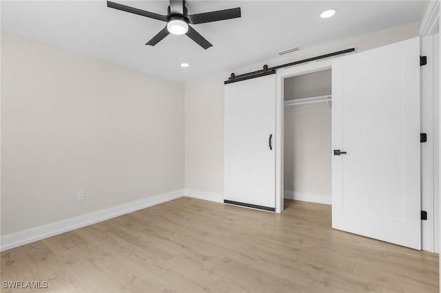 unfurnished bedroom with ceiling fan, a closet, a barn door, and light hardwood / wood-style flooring