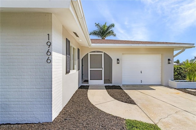 entrance to property featuring concrete driveway, brick siding, an attached garage, and a shingled roof