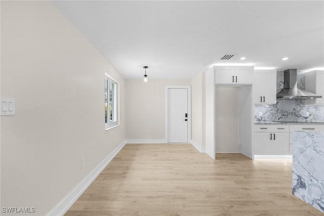 kitchen featuring wall chimney exhaust hood, white cabinetry, light wood-style flooring, and backsplash