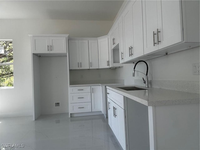 kitchen with a sink, marble finish floor, and white cabinets