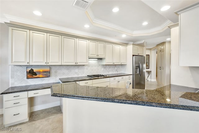 kitchen featuring a raised ceiling, appliances with stainless steel finishes, dark stone counters, and kitchen peninsula