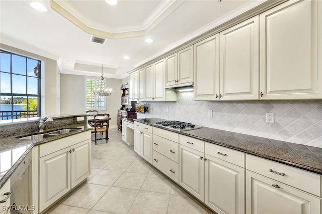 kitchen with dark stone counters, a tray ceiling, decorative light fixtures, and sink