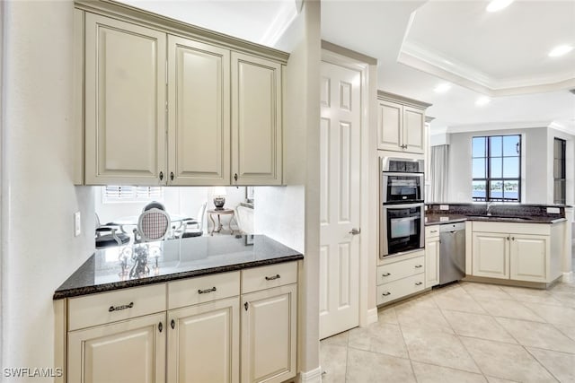 kitchen with appliances with stainless steel finishes, dark stone countertops, kitchen peninsula, a raised ceiling, and crown molding