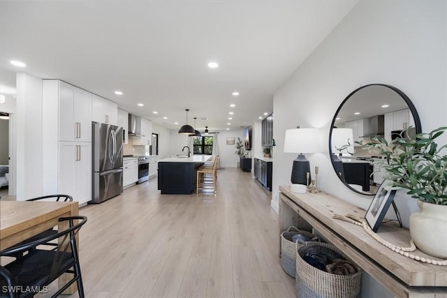 interior space featuring decorative light fixtures, white cabinetry, sink, stainless steel appliances, and a center island with sink