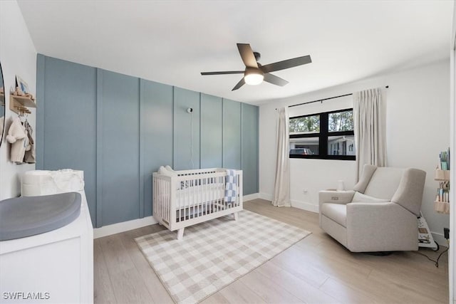 bedroom featuring ceiling fan, light hardwood / wood-style flooring, and a crib