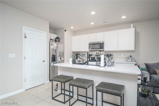 kitchen with light tile patterned flooring, stainless steel appliances, white cabinets, and a kitchen bar