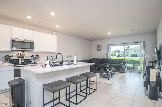 kitchen featuring light tile patterned flooring, a breakfast bar, a center island with sink, appliances with stainless steel finishes, and white cabinets