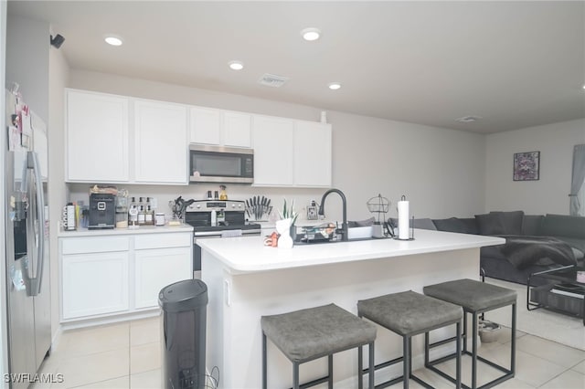 kitchen with white cabinetry, an island with sink, a kitchen breakfast bar, light tile patterned floors, and stainless steel appliances