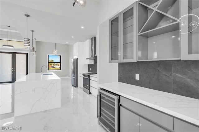 kitchen featuring wall chimney exhaust hood, decorative light fixtures, appliances with stainless steel finishes, beverage cooler, and light stone countertops