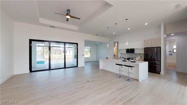 kitchen with a breakfast bar area, hanging light fixtures, black appliances, kitchen peninsula, and a raised ceiling