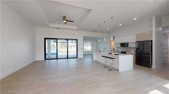 kitchen with decorative light fixtures, a breakfast bar area, a raised ceiling, black fridge, and a center island with sink