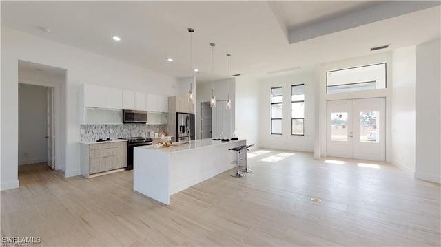 kitchen featuring hanging light fixtures, a center island with sink, white cabinets, stainless steel appliances, and backsplash