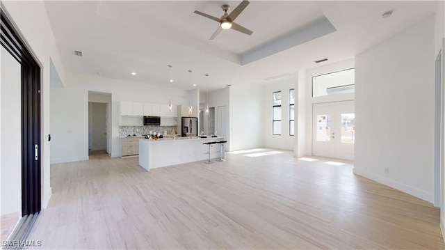 unfurnished living room featuring french doors, ceiling fan, a raised ceiling, and light hardwood / wood-style floors