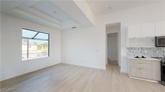 kitchen featuring light hardwood / wood-style flooring, stainless steel appliances, white cabinets, decorative backsplash, and a raised ceiling