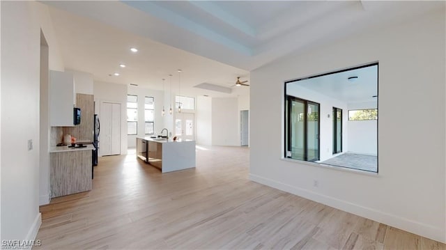 interior space featuring a raised ceiling, ceiling fan, sink, and light wood-type flooring