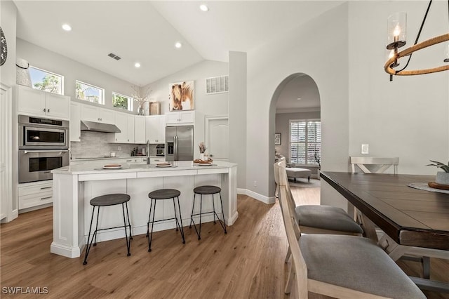 kitchen featuring appliances with stainless steel finishes, white cabinetry, tasteful backsplash, light hardwood / wood-style floors, and a kitchen bar