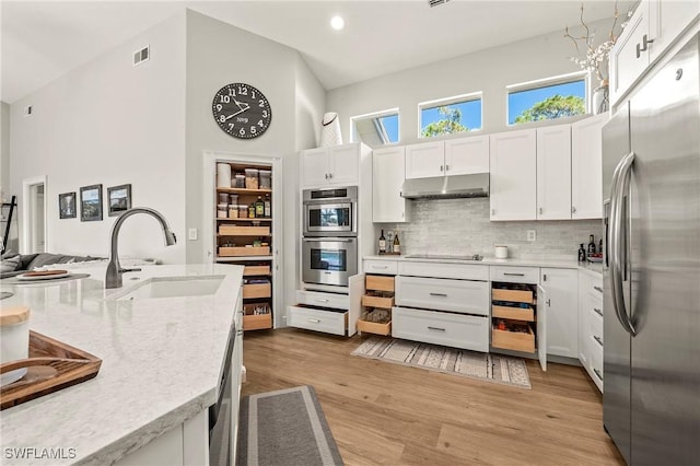 kitchen with sink, backsplash, stainless steel appliances, light hardwood / wood-style floors, and white cabinets