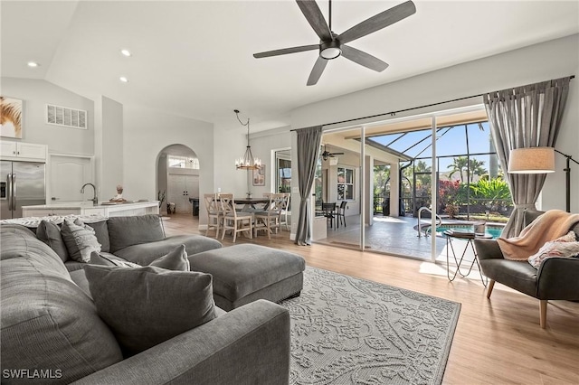 living room with ceiling fan with notable chandelier, high vaulted ceiling, and light wood-type flooring