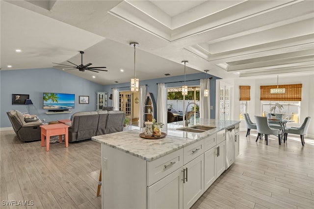 kitchen with white cabinetry, sink, hanging light fixtures, light stone countertops, and a center island with sink