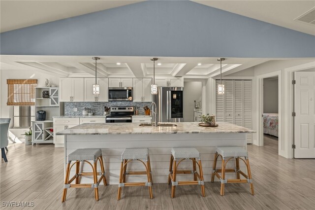 kitchen featuring stainless steel appliances, a sink, white cabinetry, a center island with sink, and pendant lighting