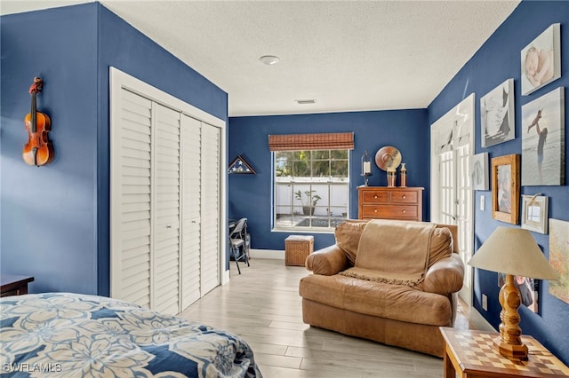 bedroom with baseboards, visible vents, a textured ceiling, light wood-type flooring, and a closet