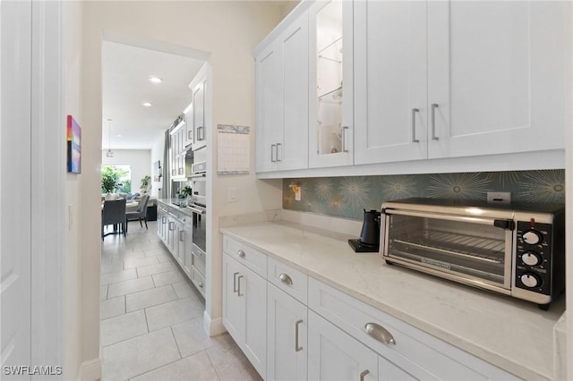 kitchen featuring light stone counters, stainless steel oven, tasteful backsplash, light tile patterned floors, and white cabinets