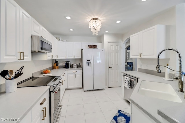 kitchen with sink, light tile patterned floors, appliances with stainless steel finishes, white cabinetry, and an inviting chandelier