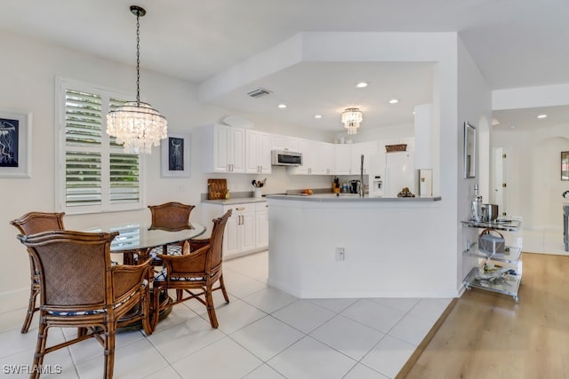 kitchen featuring light tile patterned floors, white cabinetry, white fridge with ice dispenser, decorative light fixtures, and kitchen peninsula