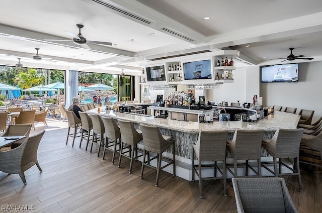 bar with beam ceiling, wood-type flooring, ceiling fan, and light stone counters