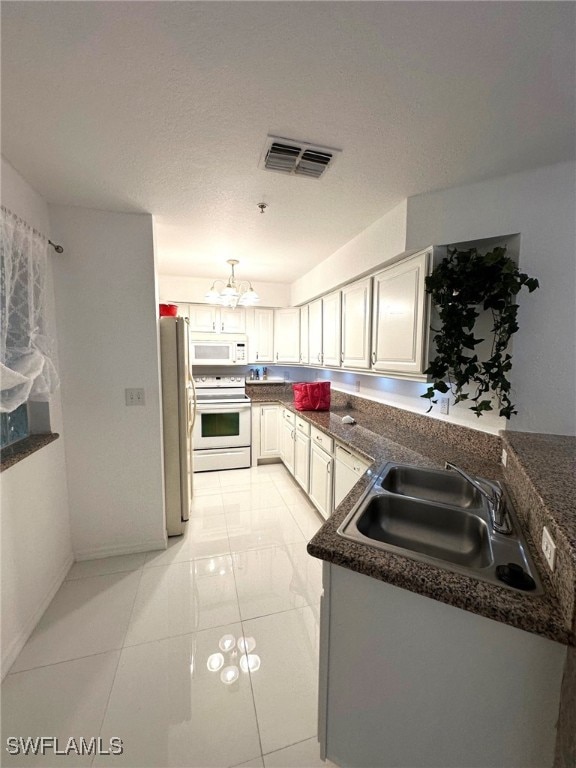 kitchen featuring light tile patterned flooring, sink, dark stone countertops, white cabinets, and white appliances