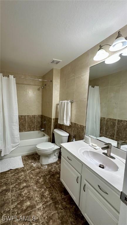 full bathroom with shower / tub combo with curtain, tile walls, vanity, a textured ceiling, and toilet