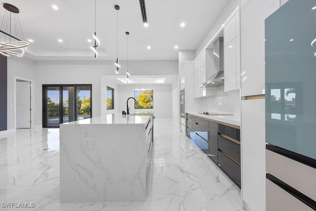 kitchen with wall chimney exhaust hood, sink, white cabinetry, a large island with sink, and pendant lighting