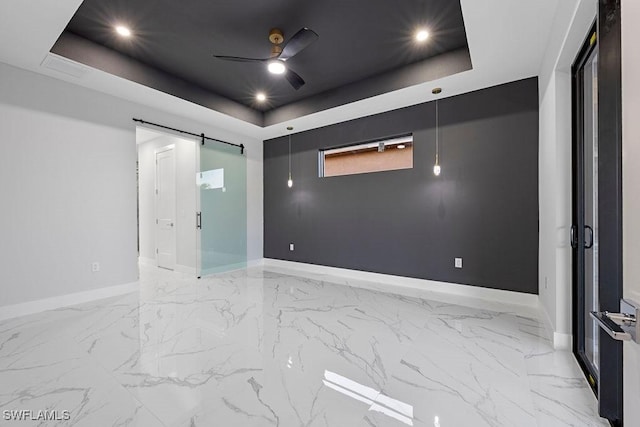 unfurnished room with a raised ceiling, ceiling fan, and a barn door