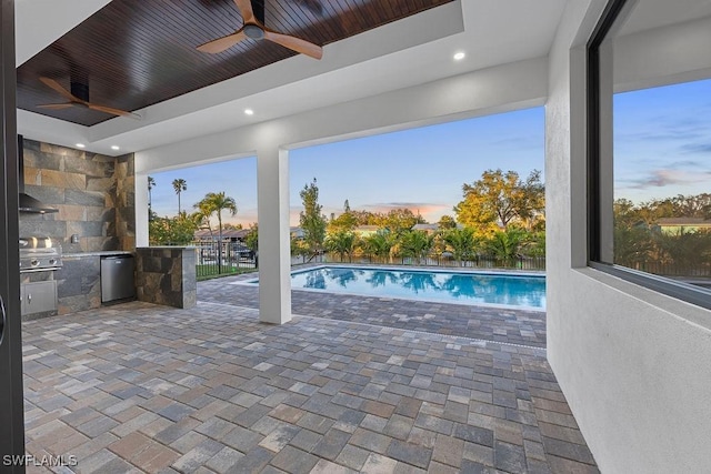 pool at dusk featuring grilling area, an outdoor kitchen, ceiling fan, and a patio