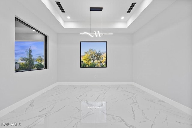 unfurnished room featuring a raised ceiling, a wealth of natural light, and a chandelier