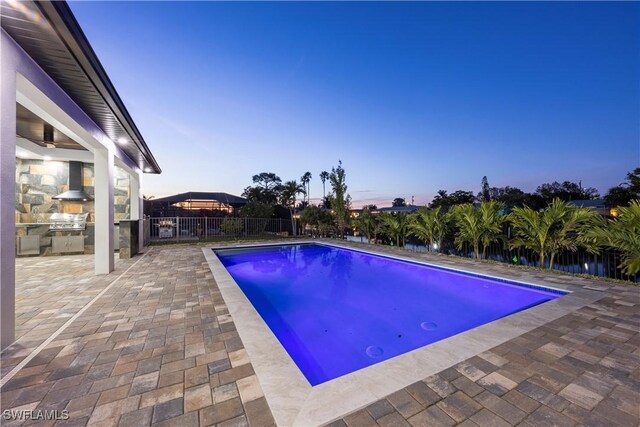 pool at dusk with an outdoor kitchen and a patio area