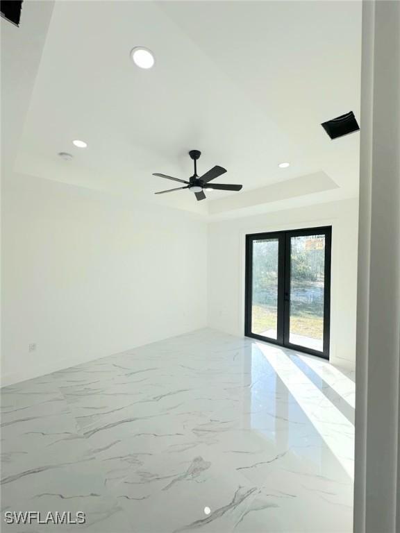 spare room with a tray ceiling, marble finish floor, ceiling fan, and french doors