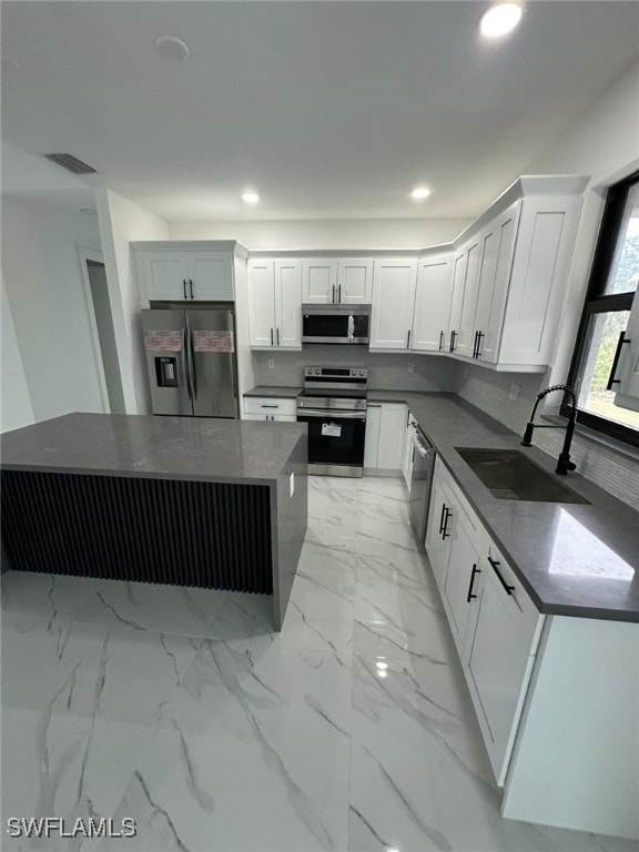 kitchen with sink, appliances with stainless steel finishes, a kitchen island, dark stone counters, and white cabinets