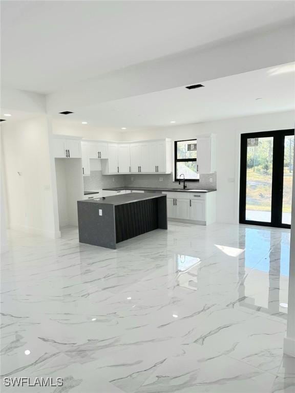 kitchen featuring a kitchen island, a sink, white cabinets, marble finish floor, and tasteful backsplash
