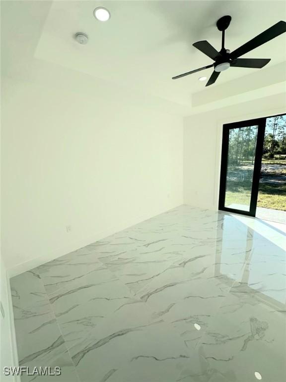 unfurnished room with recessed lighting, a raised ceiling, marble finish floor, and a ceiling fan
