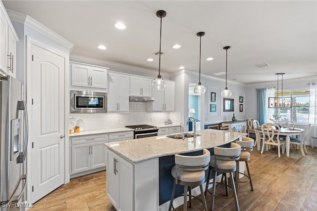 kitchen featuring decorative light fixtures, white cabinetry, a breakfast bar area, stainless steel appliances, and a center island with sink