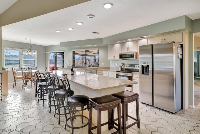 kitchen featuring a breakfast bar, visible vents, hanging light fixtures, appliances with stainless steel finishes, and white cabinetry