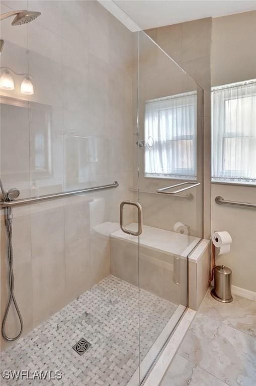 bathroom featuring marble finish floor, a shower stall, and a healthy amount of sunlight