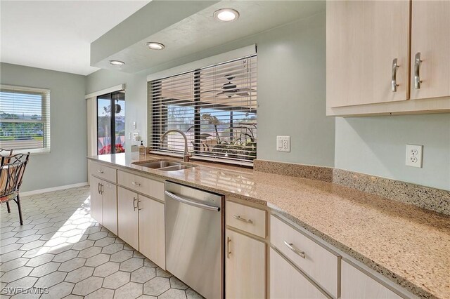 kitchen featuring recessed lighting, stainless steel dishwasher, a sink, light stone countertops, and baseboards