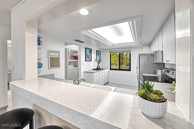 kitchen featuring stainless steel appliances, a breakfast bar, white cabinets, and washer and clothes dryer