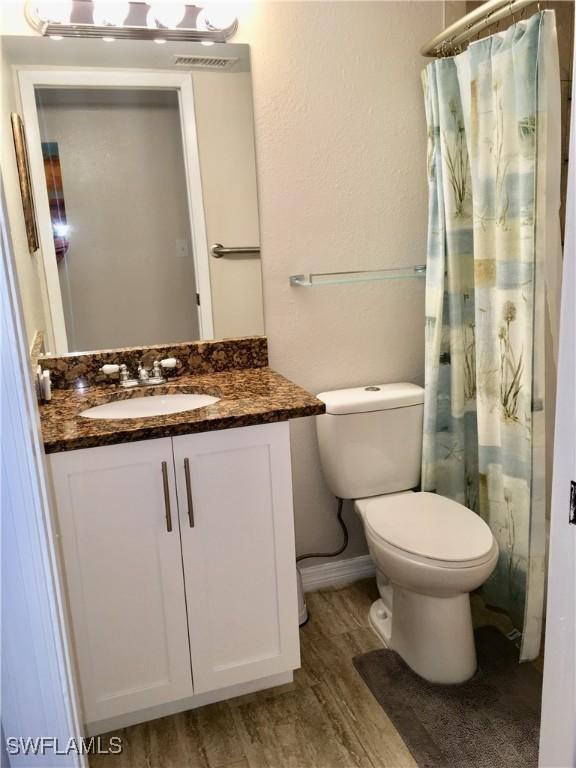 bathroom with walk in shower, wood-type flooring, toilet, and vanity