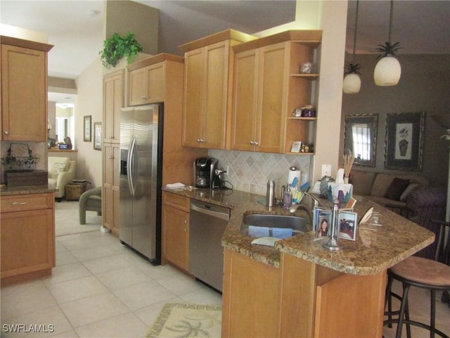 kitchen featuring appliances with stainless steel finishes, a breakfast bar, backsplash, light stone counters, and kitchen peninsula