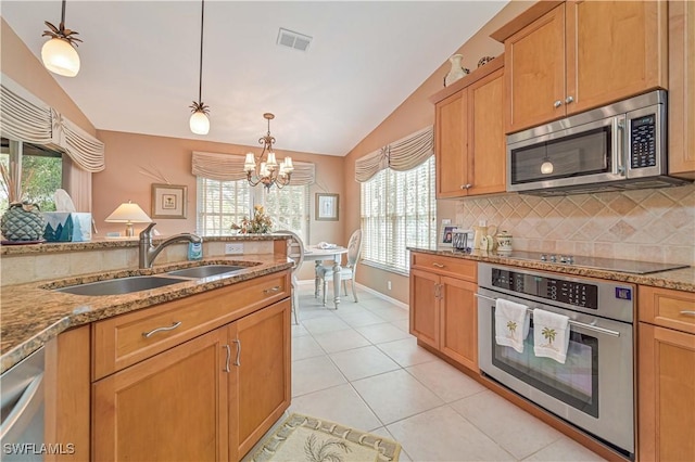 kitchen featuring lofted ceiling, sink, light stone counters, pendant lighting, and stainless steel appliances